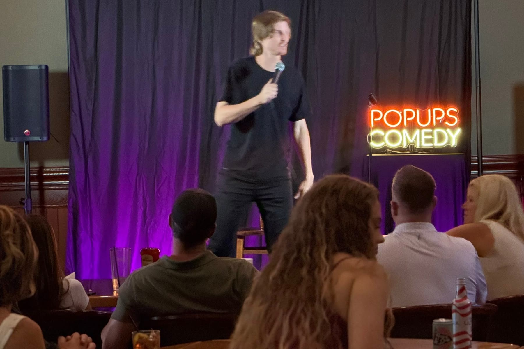 A packed room watching a comic at a Popups Comedy show